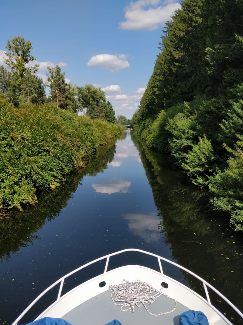 A still forest canal mirroring the clouds — view from Tom Cat's bow